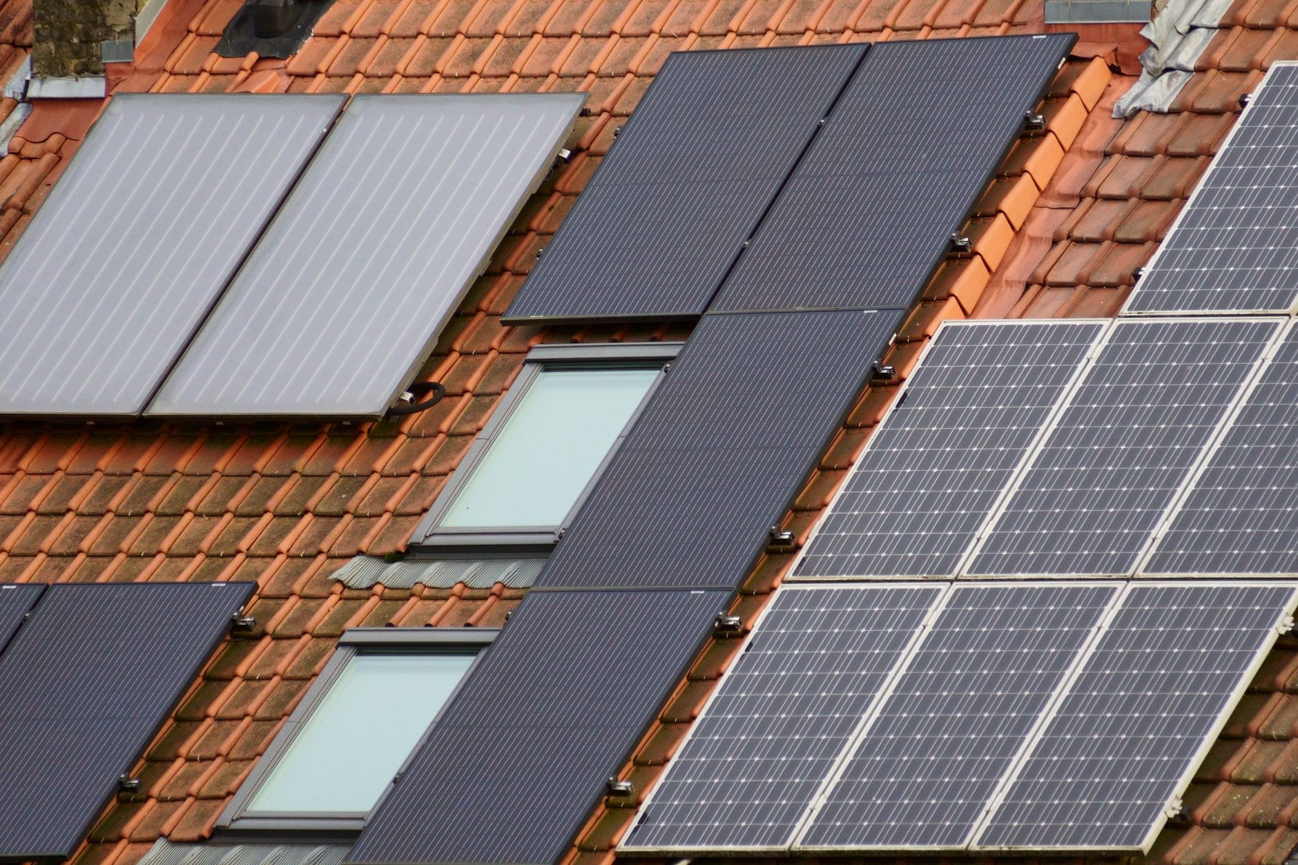 Capteurs solaires thermiques plans posés sur une toiture en tuiles, à côté de panneaux photovoltaïques