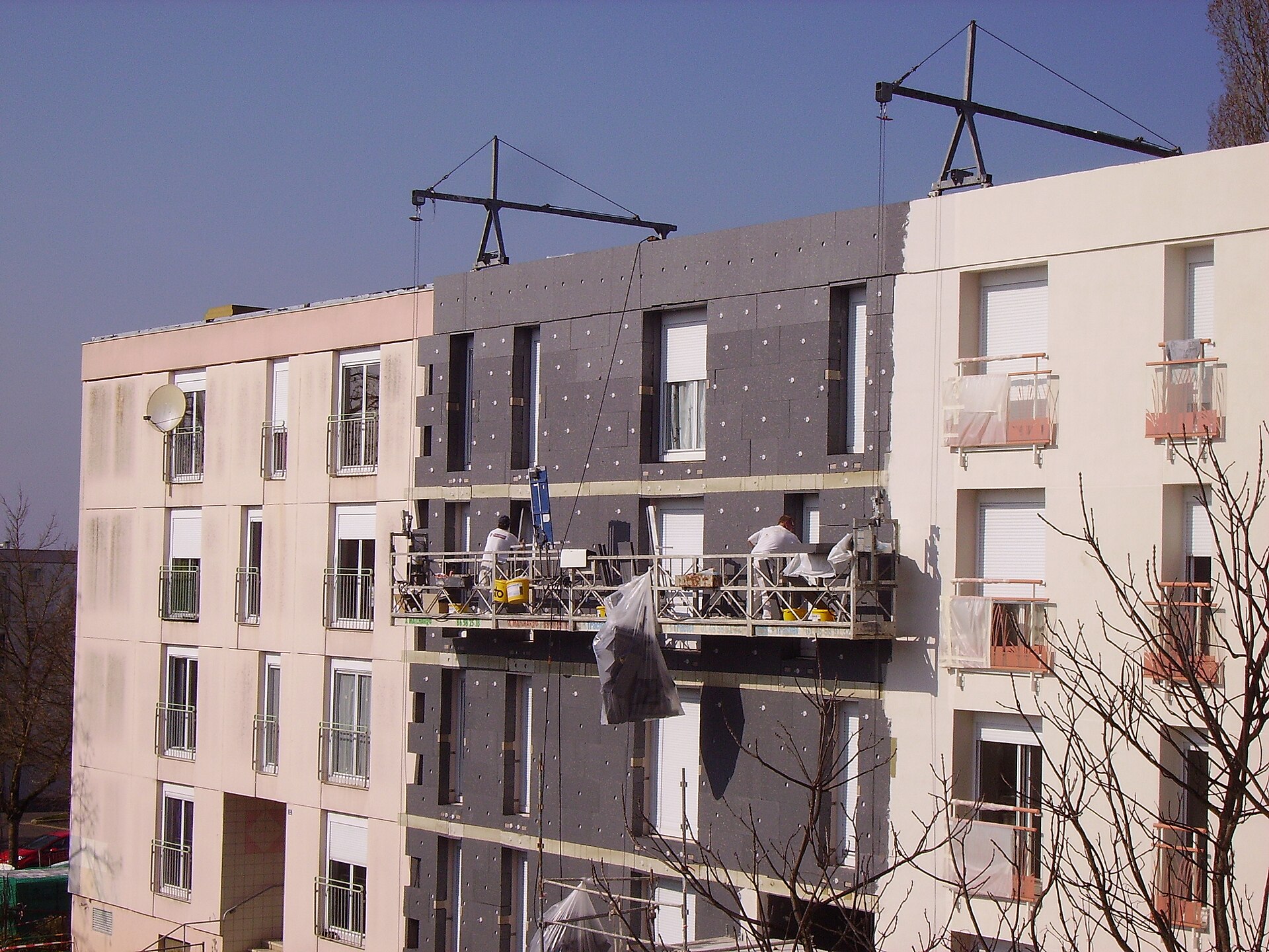 panneaux d'isolant posés sur la façade d'un immeuble, nacelle de chantier et ouvriers au travail