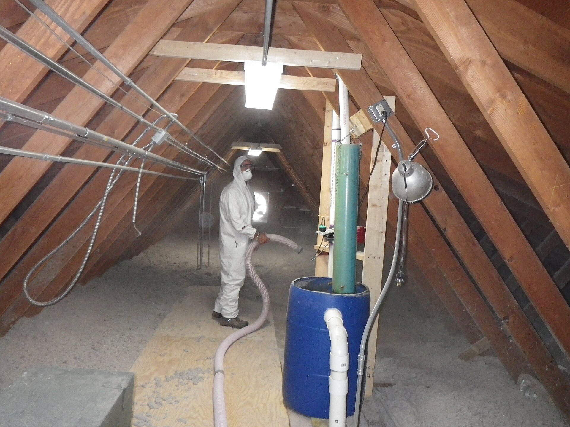 technicien en combinaison soufflant de l'isolant en vrac sur le plancher d'un grenier sous charpente en bois
