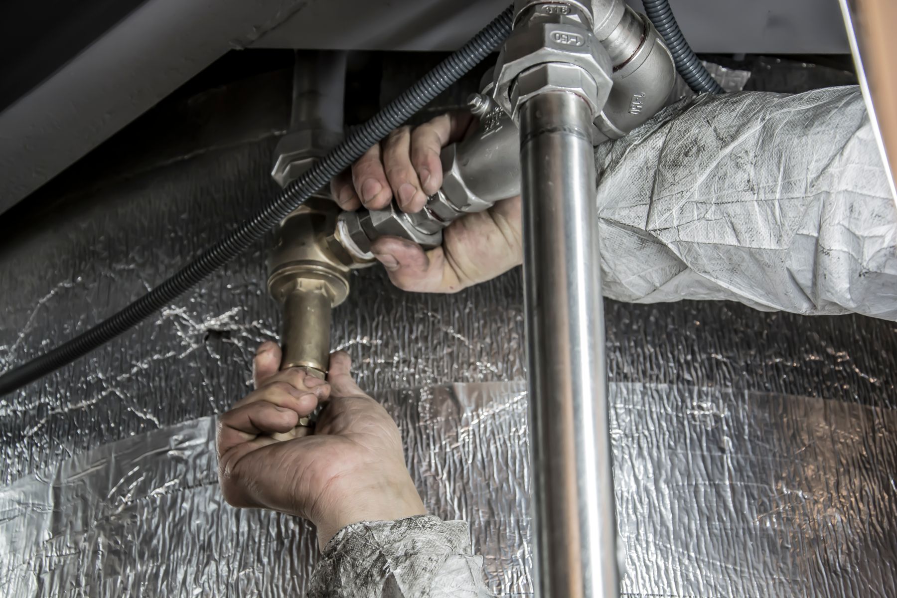 mains d'un technicien serrant des raccords de canalisation sous un appareil